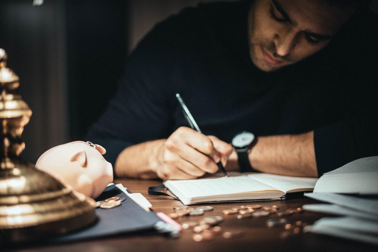 man writing in account book at table